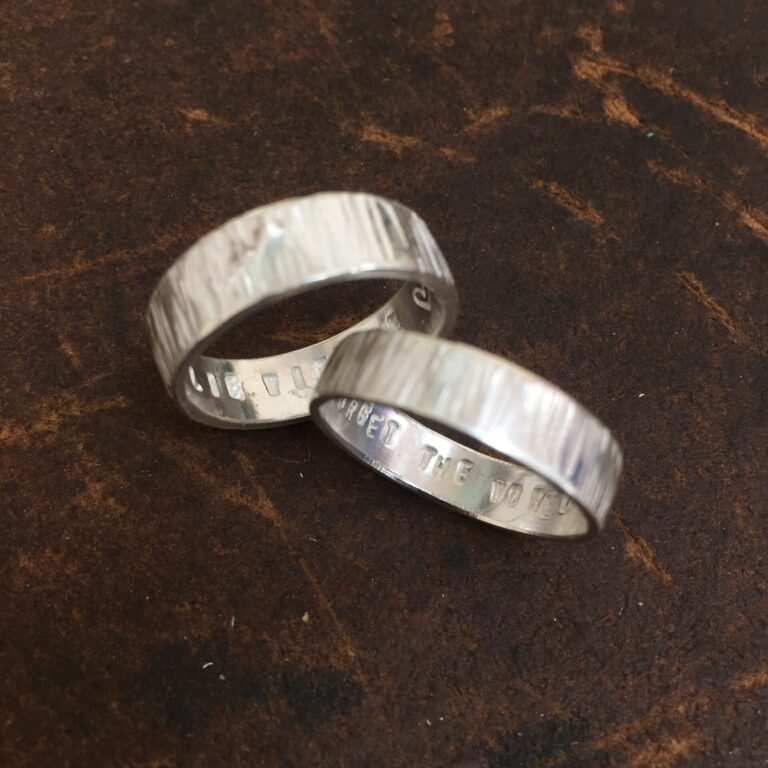 two bright silver rings against a dark background. The rings have a linear texture hammered into them making the surface appear like bark.