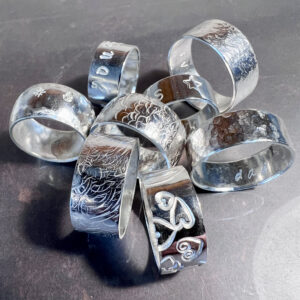 handmade silver rings with hammer textures and stamped with words and symbols.